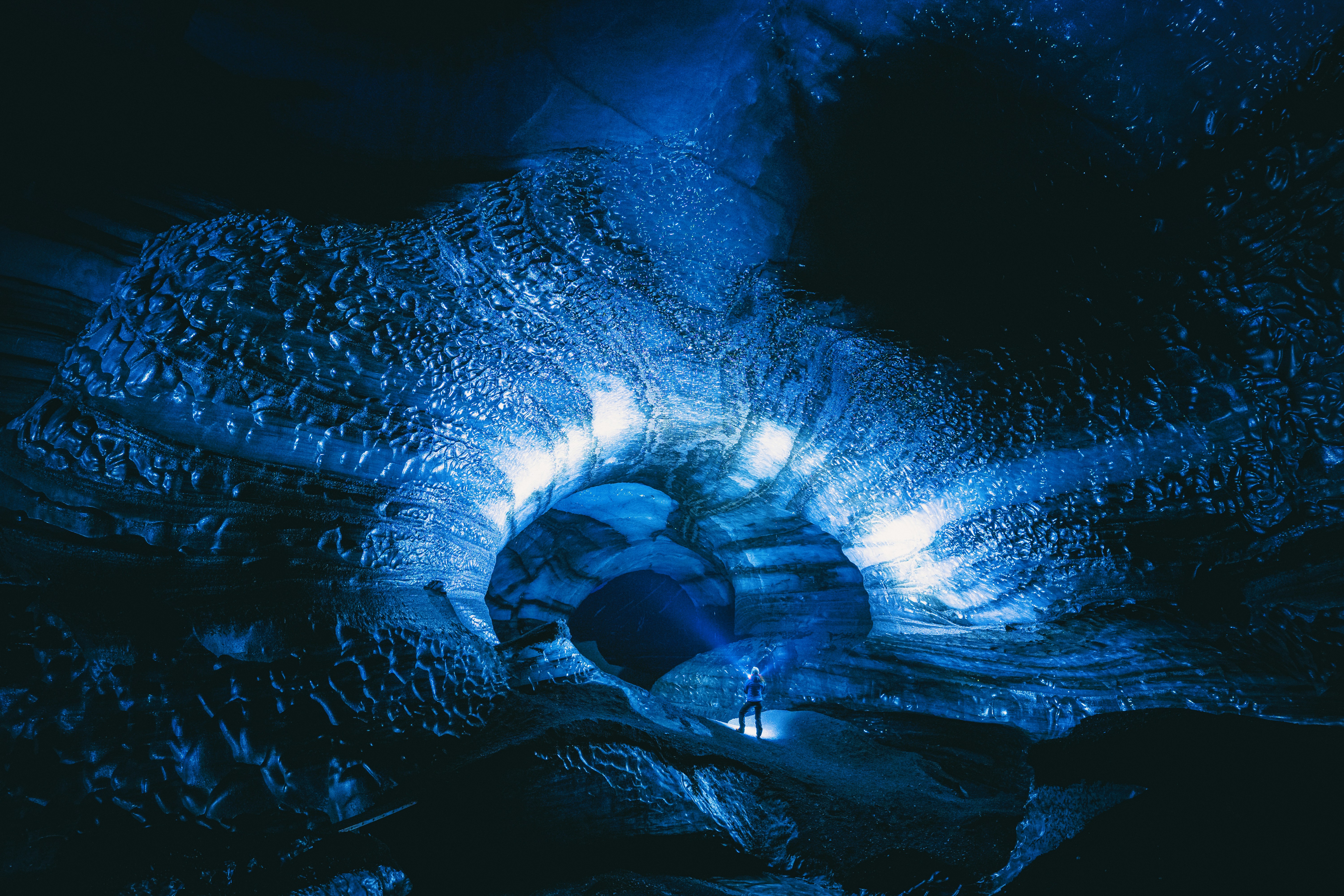 Dramatic blue ice cave interior with sunlight filtering through translucent glacier ice walls